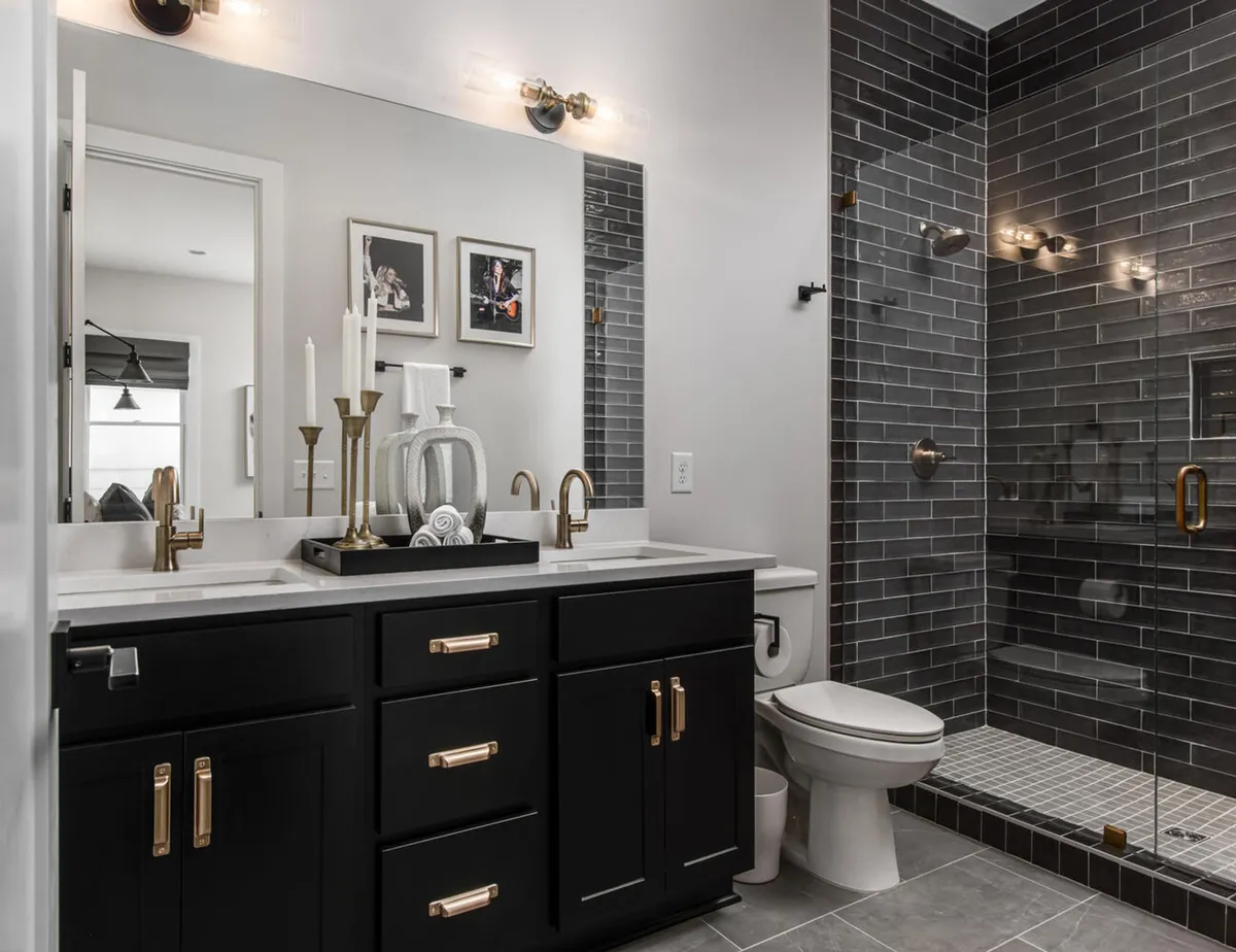 An elegant bathroom featuring black cabinetry, gold fixtures, a large mirror, a glass shower enclosure, and decorative candles. The room radiates calm and sophistication, ideal for moments of self-care.