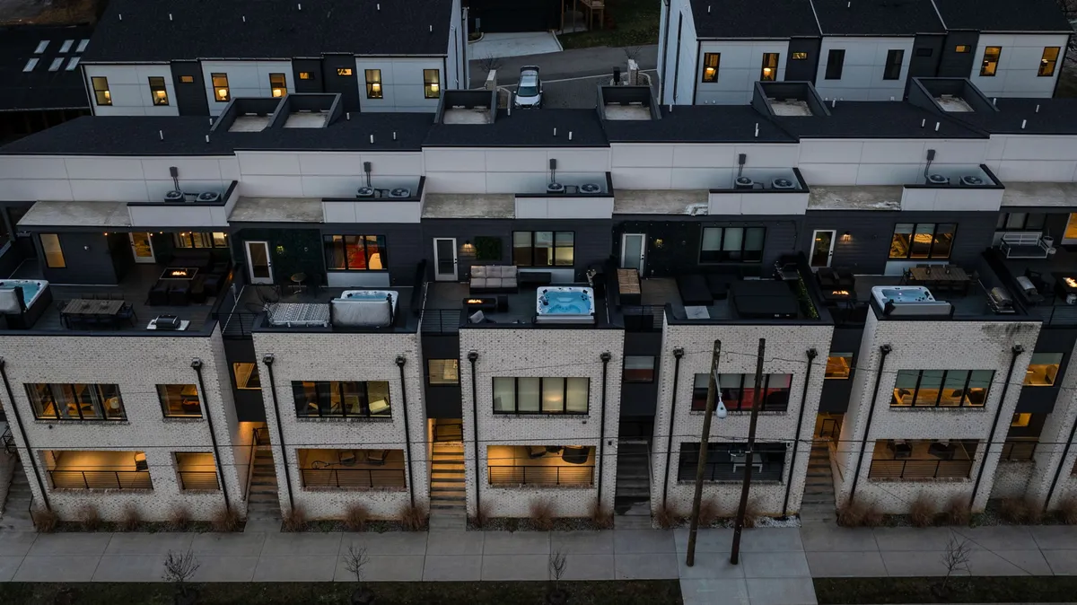 A contemporary rooftop patio featuring comfortable outdoor furniture, hot tubs, and stylish architectural details. The setting overlooks city views and has intimate lighting, creating a luxurious, inviting atmosphere for evening gatherings or celebrations under the stars.