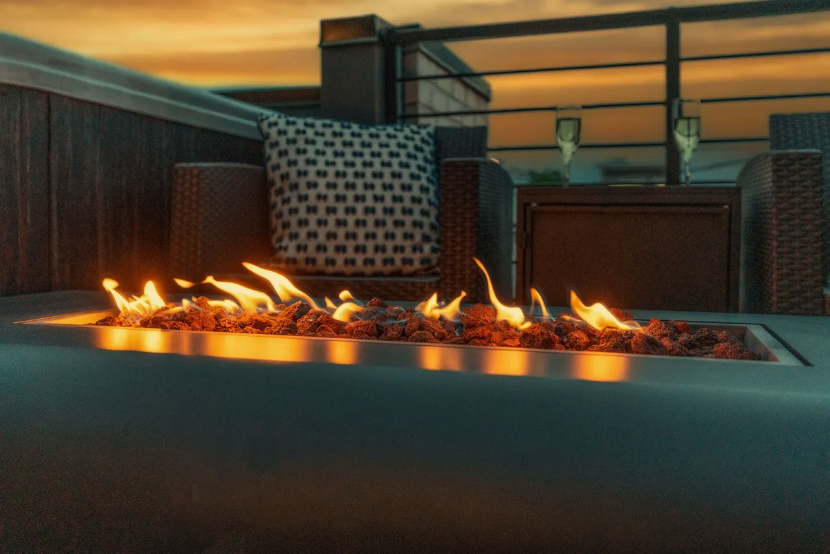 An outdoor scene with a glowing fire pit, plush outdoor furniture, and champagne glasses set out, suggesting an atmosphere of relaxation and celebration at sunset. The environment is serene and perfect for toasting special occasions or enjoying an evening with friends.