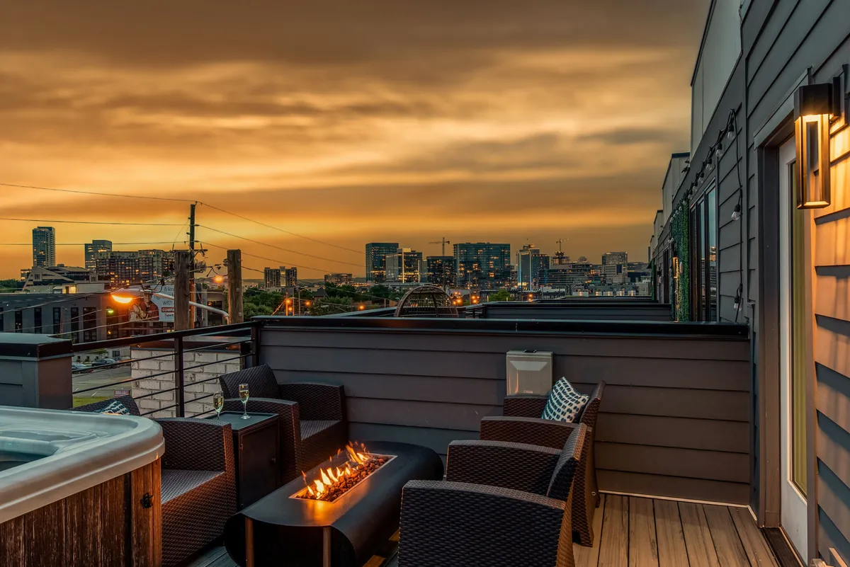 A stylish rooftop deck at sunset, featuring a cozy fire pit surrounded by comfortable outdoor seating. The city skyline forms a dramatic backdrop, and the sky glows with the colors of dusk, setting the scene for relaxing, social evenings above the urban buzz.