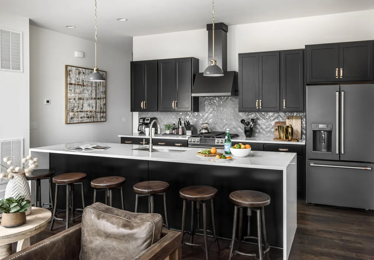 A contemporary kitchen featuring a large marble-topped island with bar seating, dramatic black cabinetry, stainless steel appliances, and decorative artwork. The space is well-lit and open, inviting group meal prep, entertaining, and casual dining.