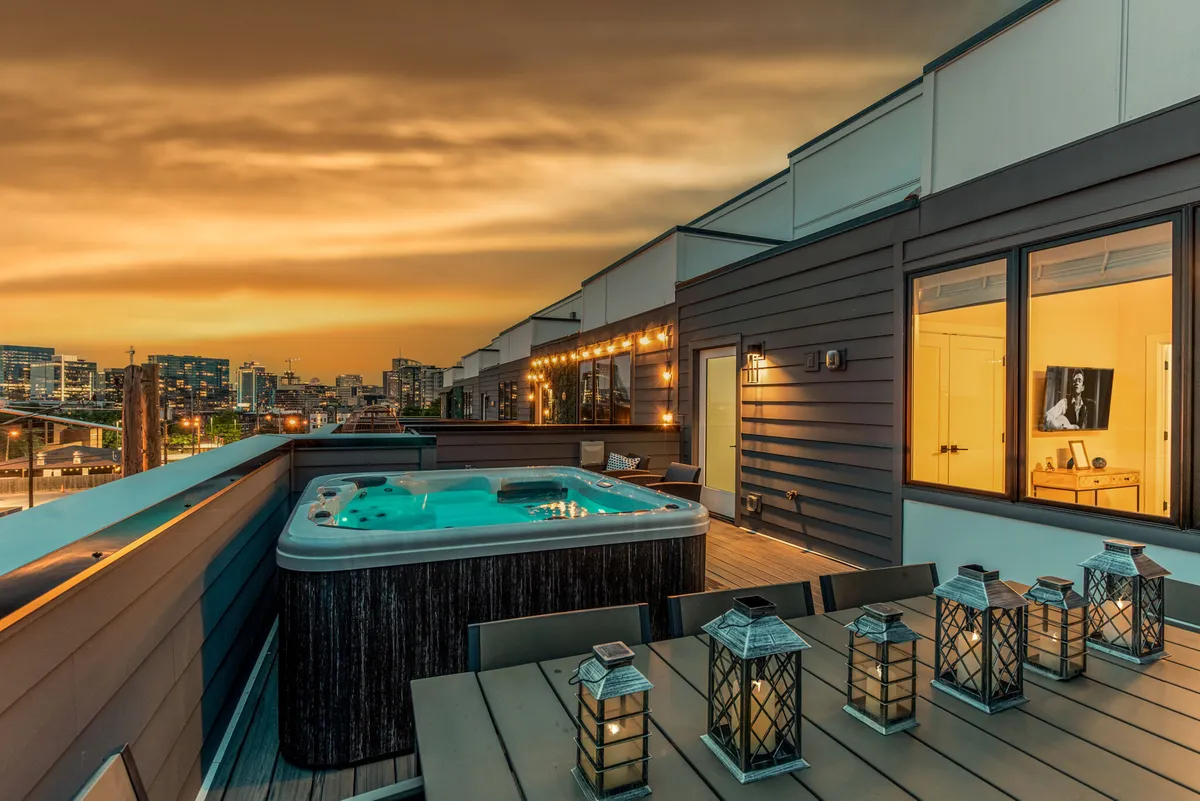 A luxurious rooftop setting with a hot tub, elegant outdoor dining table, and sweeping city skyline views. Warm lighting creates a tranquil yet sophisticated mood, perfect for relaxing or entertaining friends under the stars.