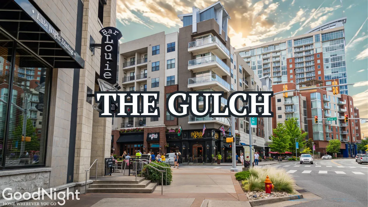 An energetic exterior street scene featuring the Bar Louie sign, apartment buildings, pedestrian traffic, and lush green landscaping. The area looks inviting, with people dining and socializing, encapsulating the active, urban lifestyle.