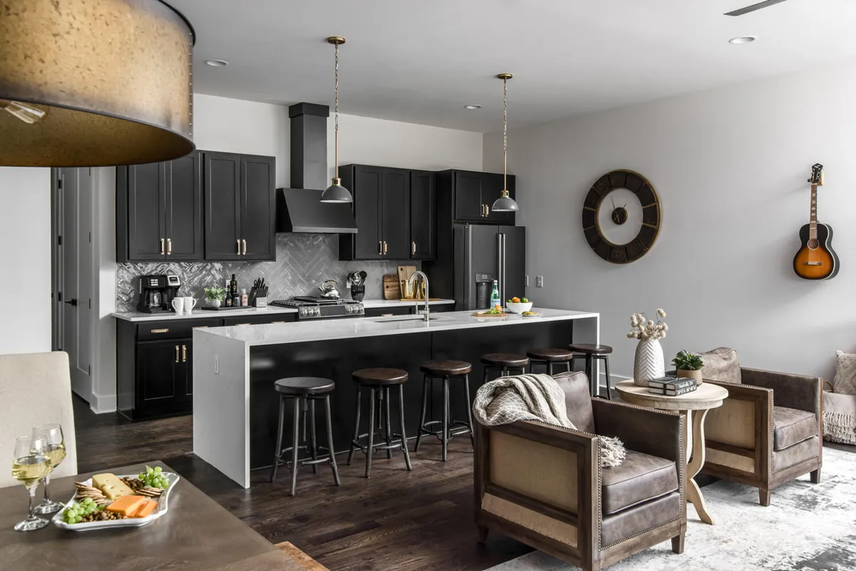A welcoming kitchen with a large island and bar stools, accented by a wall-mounted guitar and prominent clock. The space balances cozy ambiance with modern finishes, ideal for intimate gatherings or casual breakfasts.