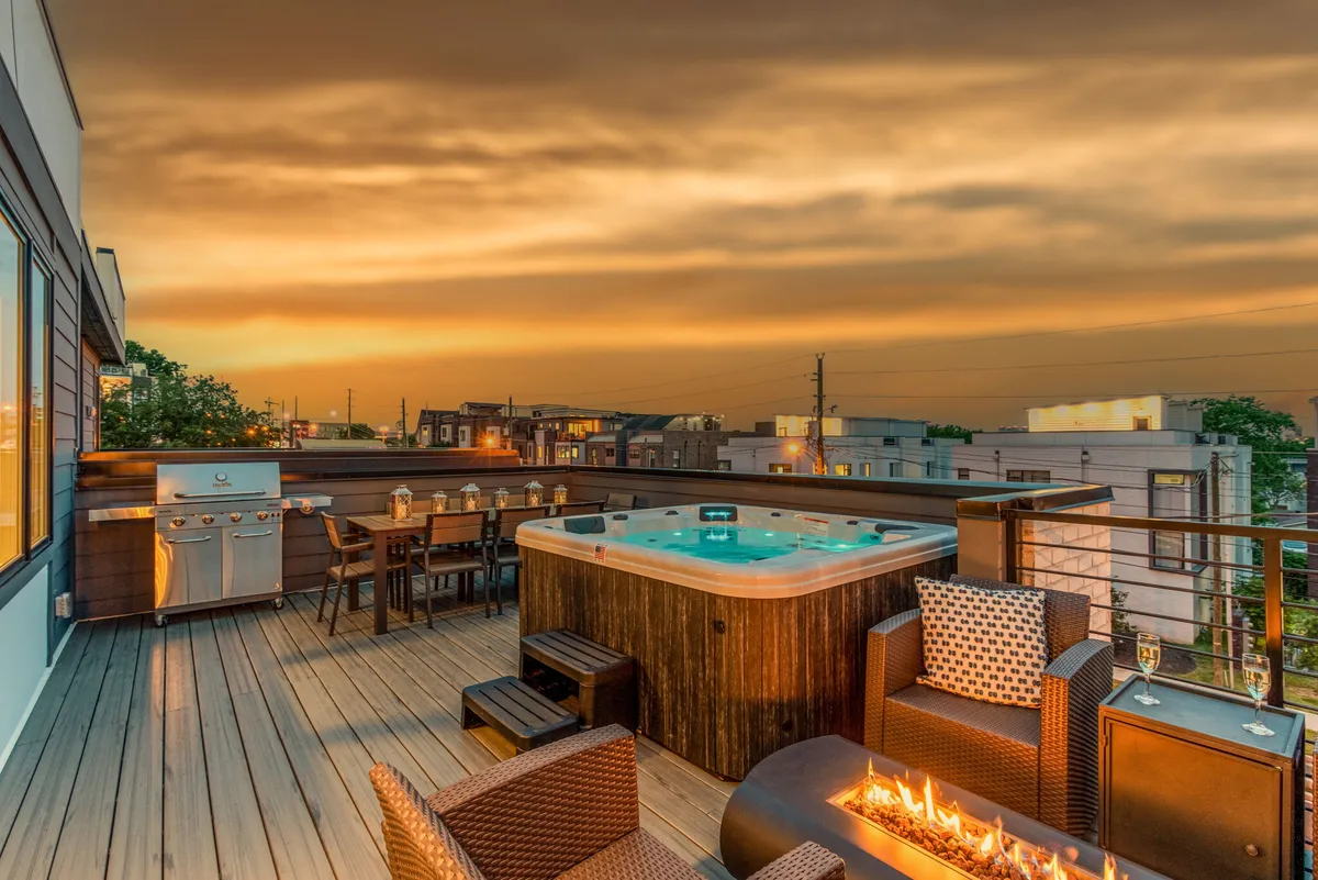 An exterior space featuring a hot tub, fire pit, dining area, and grill. The area is set up for both relaxing and socializing, with amenities that encourage outdoor dining, soaking in the hot tub, and enjoying evenings under the stars.